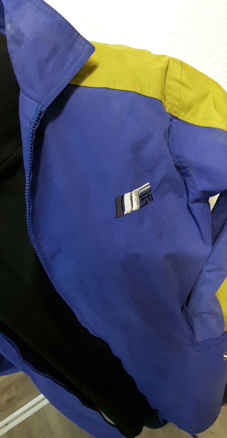May include: A blue and yellow jacket with a black interior. The jacket has a zipper closure and a small logo on the chest. The collar is blue, and the shoulders are yellow.