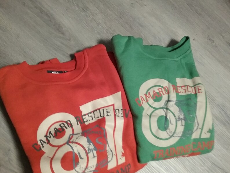 May include: Two sweatshirts, one red and one green, with the text "Camaro Rescue" and the number "87" printed on them. Both sweatshirts have a distressed, vintage look.