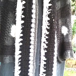 May include: A black and white crochet shawl and scarf set. The shawl is dark with white accents, and the scarf has a white, textured border. The set is handmade and appears to be warm and cosy.
