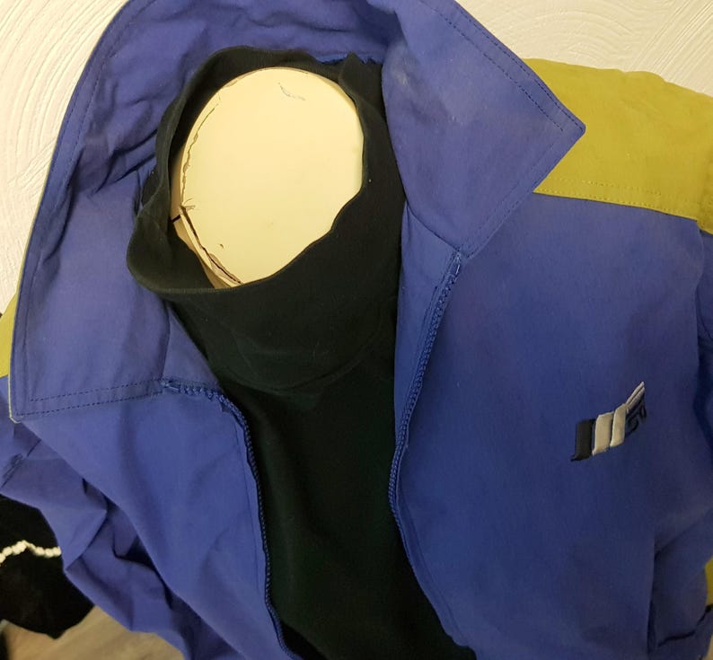 May include: A blue and yellow jacket with a black turtleneck. The jacket has a zipper and a logo on the front. The jacket is displayed on a mannequin.