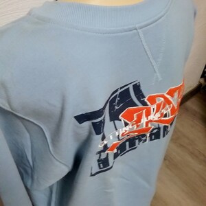 May include: Light blue sweatshirt with a graphic print of a red, white, and blue design. The design includes the text "Getting There" and a stylized image of a basketball.
