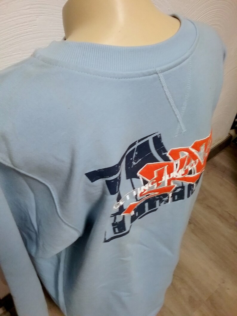 May include: Light blue sweatshirt with a graphic print of a red, white, and blue design. The design includes the text "Getting There" and a stylized image of a basketball.