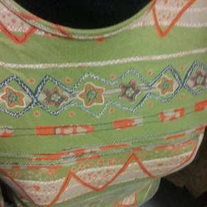 Könnte beinhalten: Grün-oranges gestreiftes Shirt mit geometrischem Muster. Das Shirt hat einen runden Ausschnitt und eine Strickstruktur.