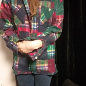 Könnte beinhalten: Ein langärmliges Karohemd mit Patchwork-Muster in Rot-, Grün-, Blau- und Gelbtönen. Das Hemd ist aus einem weichen, flanellartigen Stoff.