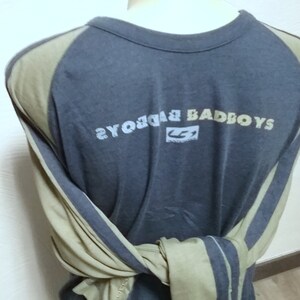 May include: A long-sleeved shirt with a gray body and tan sleeves. The shirt has a graphic print on the back that says "Badboys" with a logo underneath. The sleeves have a stripe design.