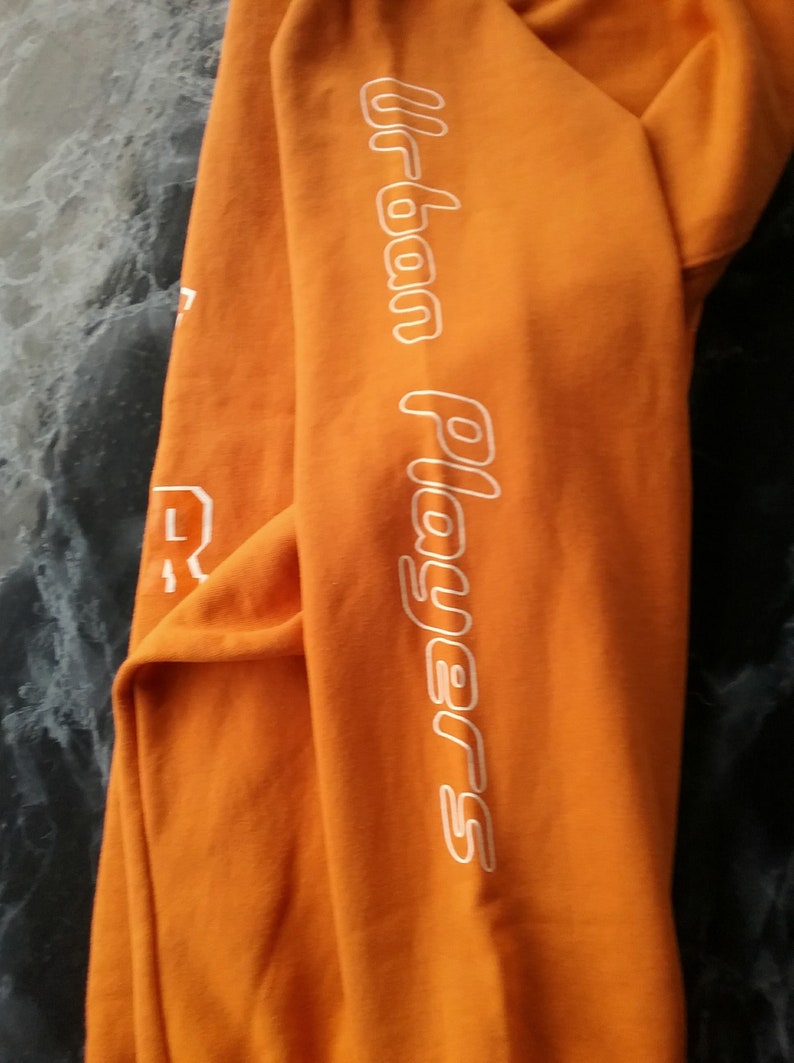 Op de afbeelding: Oranje sweatshirt met witte tekst "Urban Players" op de mouw.
