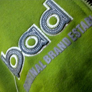 May include: A green zippered jacket with a white embroidered logo that says "bad original brand establ"