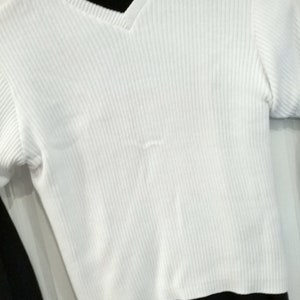 Peut inclure: Haut blanc en tricot côtelé avec un col en V et des manches courtes. Le haut est fait d'un tissu doux et texturé. La chemise est de couleur blanche unie et semble être de style décontracté.