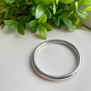 May include: A silver bangle bracelet with a smooth, rounded surface.