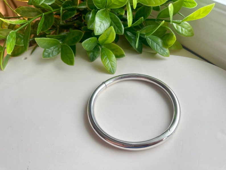May include: A silver bangle bracelet with a smooth, rounded surface.
