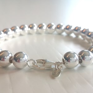 May include: A silver bracelet with a clasp fastening. The bracelet is made of round beads.