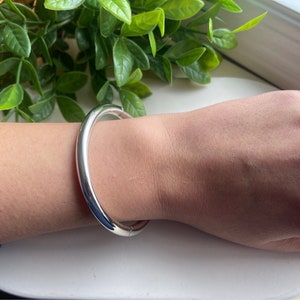 May include: A silver bangle bracelet with a smooth, rounded surface.