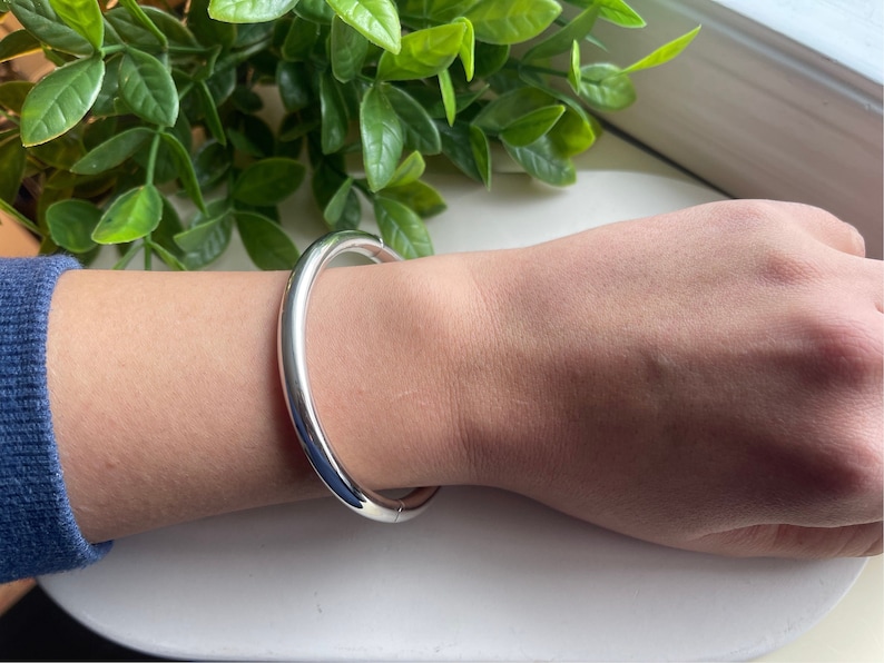 May include: A silver bangle bracelet with a smooth, rounded surface.
