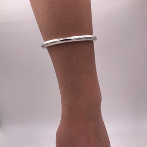 May include: A silver bangle bracelet with a smooth, rounded surface.