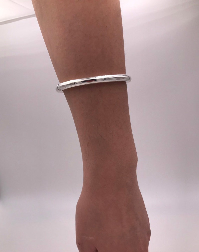 May include: A silver bangle bracelet with a smooth, rounded surface.