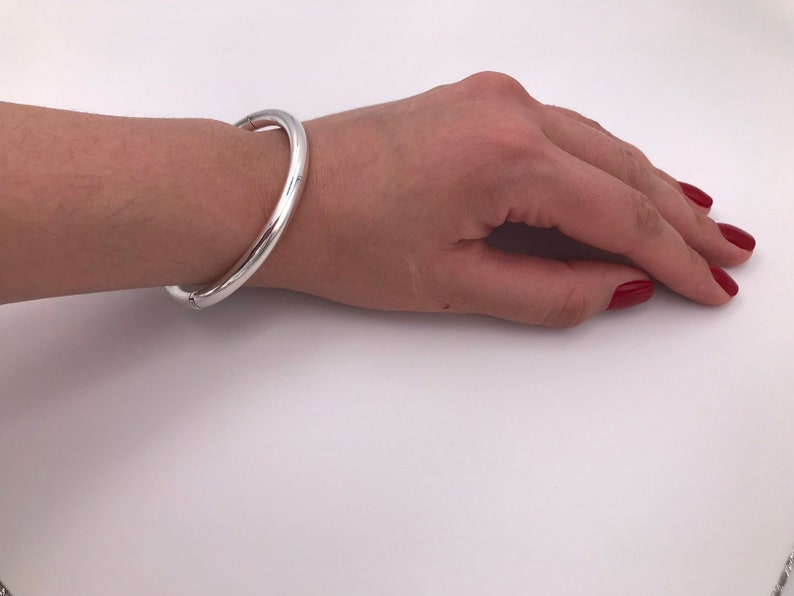 May include: A silver bangle bracelet with a smooth, polished finish. The bracelet is open and has a hinged clasp.