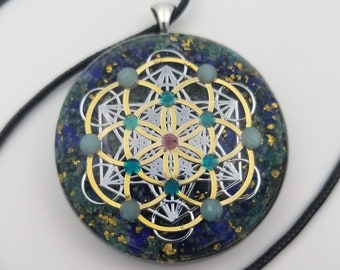 May include: A silver pendant featuring a gold-toned geometric design, surrounded by blue, green, and pink gemstones. The pendant is on a black cord.