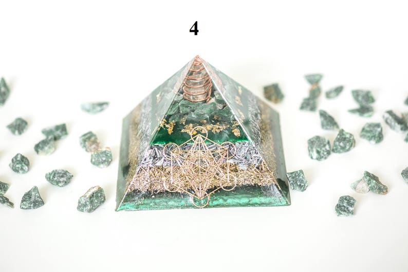 May include: A green pyramid-shaped orgone energy generator with gold accents and a copper coil at the apex. The pyramid features a geometric design and is surrounded by small green stones. The number "4" is visible at the top.