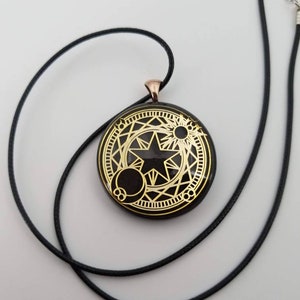 May include: A black cord necklace with a round pendant featuring a gold star and geometric design on a black background.