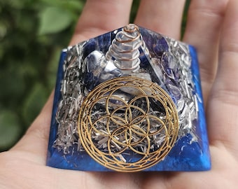 May include: A blue and silver crystal pyramid with a gold flower of life design and a clear quartz crystal point in the center.