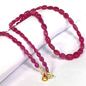 May include: A strand of pink oval-shaped beads with gold clasps. The beads are strung on a thin gold chain.