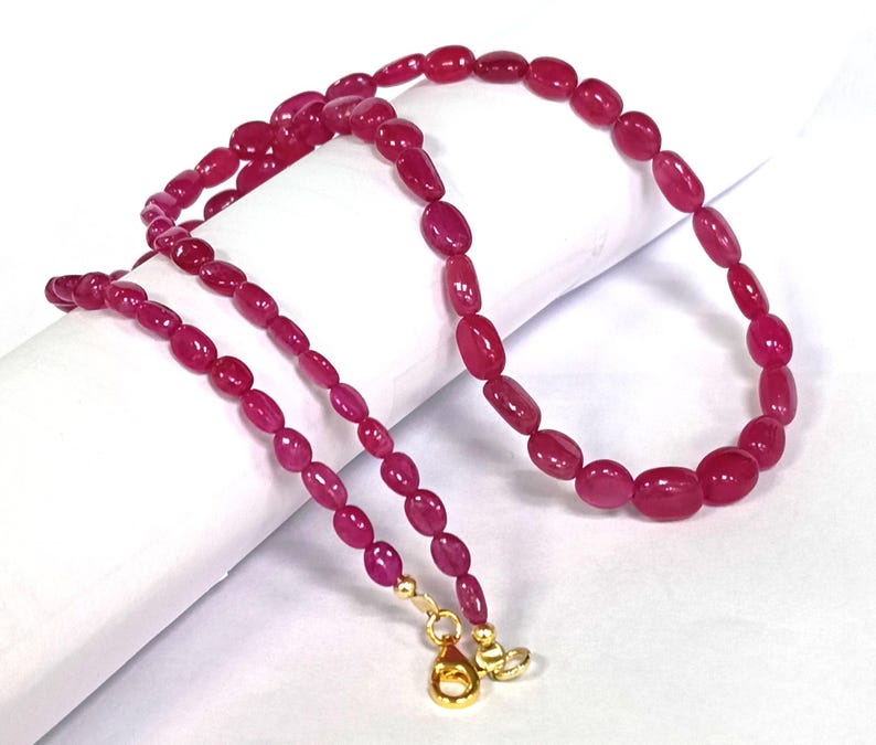 May include: A strand of pink oval-shaped beads with gold clasps. The beads are strung on a thin gold chain.