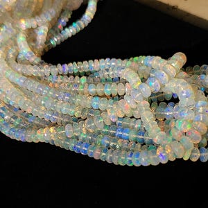 May include: Strands of iridescent opal beads. The beads are a mix of white and translucent colors, with flashes of blue, green, and yellow. The beads are strung together, creating a flowing, textured appearance. The opals are round and faceted.