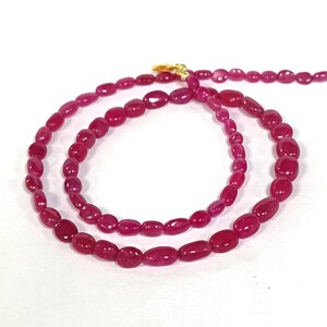 May include: A long necklace made of pink oval-shaped beads with a gold clasp.