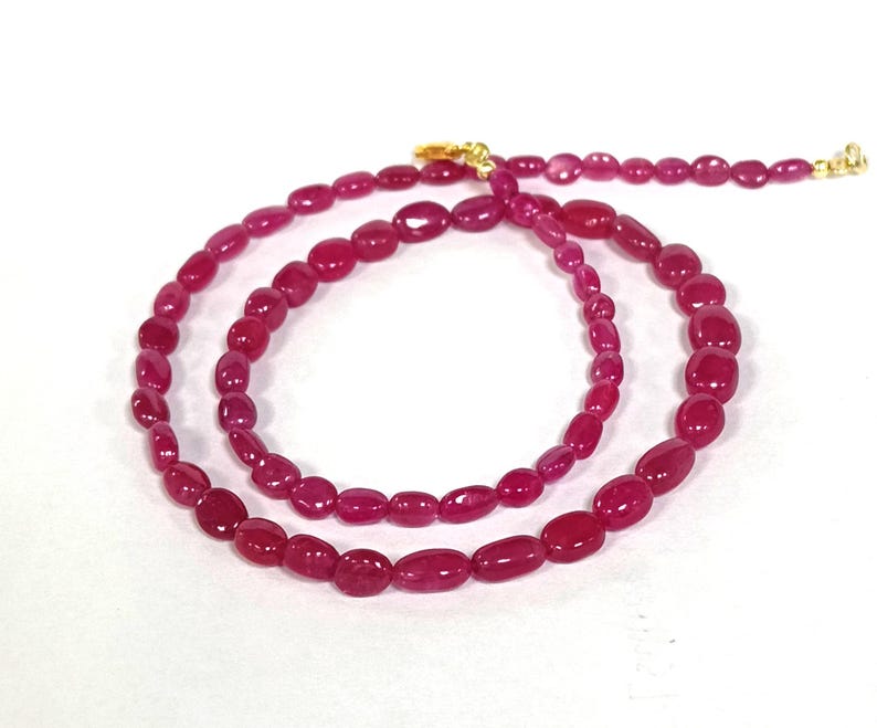 May include: A long necklace made of pink oval-shaped beads with a gold clasp.