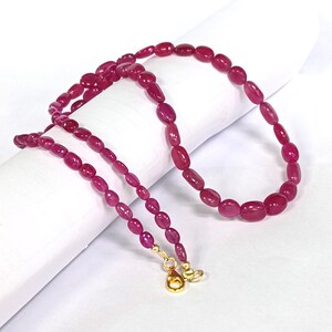 May include: A pink ruby gemstone necklace with oval-shaped beads and gold clasps.