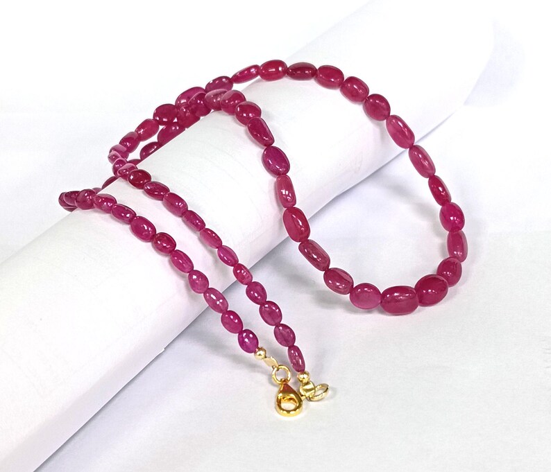 May include: A pink ruby gemstone necklace with oval-shaped beads and gold clasps.