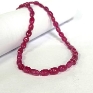 May include: A strand of oval-shaped, pink ruby beads. The beads are strung on a clear thread and are approximately 1/2 inch in length.