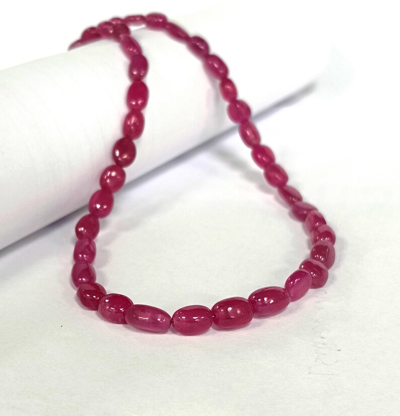 May include: A strand of oval-shaped, pink ruby beads. The beads are strung on a clear thread and are approximately 1/2 inch in length.