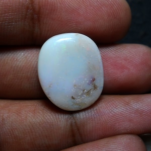 Puede incluir: Una piedra preciosa de ópalo ovalada blanca con un color blanco lechoso y algunas inclusiones marrones.