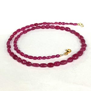 May include: A strand of pink oval-shaped gemstone beads strung on a gold chain with a clasp.