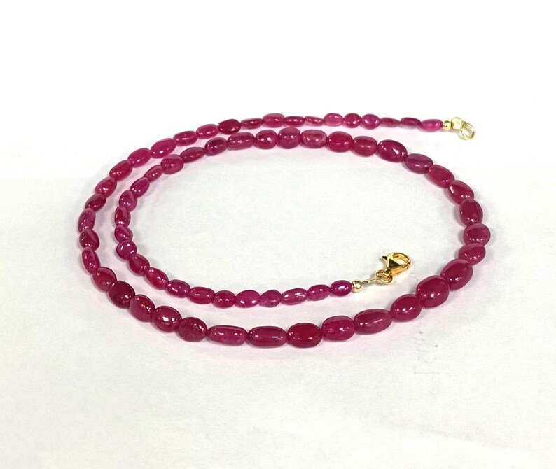 May include: A strand of pink oval-shaped gemstone beads strung on a gold chain with a clasp.