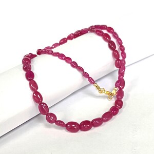 May include: A pink gemstone necklace with oval-shaped beads. The necklace is made of a string of pink gemstones with a gold clasp.
