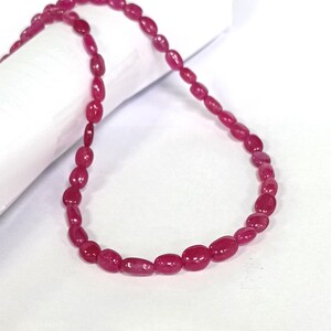 May include: A strand of pink ruby beads, strung together to form a necklace. The beads are oval shaped and have a smooth, polished finish.