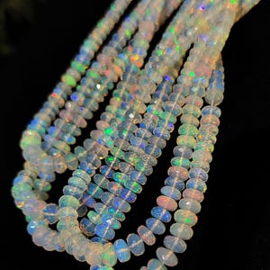 May include: Strands of faceted opal beads with iridescent flashes of color. The beads are a milky white color with hints of blue, green, and pink. The beads are strung together, creating a necklace or bracelet.