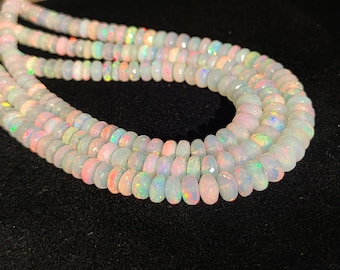 May include: A strand of white opal beads with iridescent flashes of color. The beads are faceted and have a slightly rounded shape.