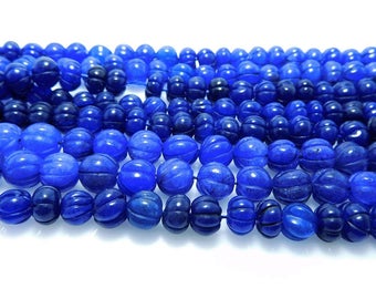 May include: A strand of blue gemstone beads with a carved, textured surface. The beads are oval shaped and have a glossy finish.