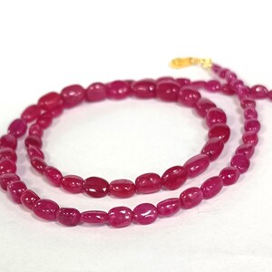 May include: A strand of pink gemstone beads, strung on a gold chain. The beads are oval shaped and have a smooth, polished finish.