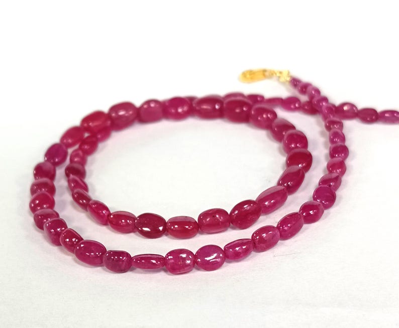 May include: A strand of pink gemstone beads, strung on a gold chain. The beads are oval shaped and have a smooth, polished finish.