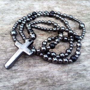 May include: A black hematite beaded necklace with a silver cross pendant. The beads are faceted and have a shiny finish. The cross is simple and elegant.