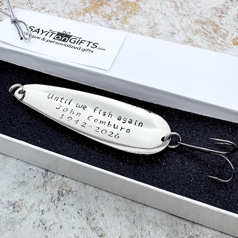 Pu&ograve; includere: Un'esca da pesca argentata con l'iscrizione "Until we fish again John Cembura 1942-2026" &egrave; presentata in una confezione regalo bianca. L'esca ha un amo ed &egrave; un regalo commemorativo.