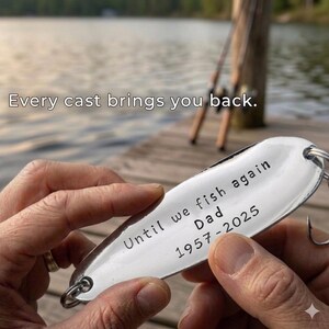 Pu&ograve; includere: Un'esca da pesca argentata con la scritta "Until we fish again Dad 1957-2025" e un amo. L'immagine include anche il testo "Every cast brings you back."