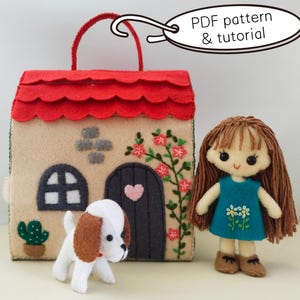 Puede incluir: Una bolsa con forma de casa de fieltro con un tejado rojo festoneado, una puerta negra con un corazón rosa y una ventana. Una muñeca de fieltro con un vestido azul y un perro de fieltro están al lado de la bolsa. El texto "PDF pattern & tutorial" está en un óvalo blanco.