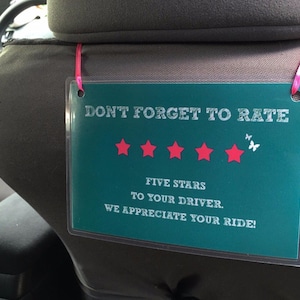 May include: A green sign with white text that reads "DON'T FORGET TO RATE" with five red stars and two white butterflies. The sign also says "FIVE STARS TO YOUR DRIVER. WE APPRECIATE YOUR RIDE!"