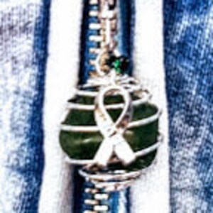 May include: A green stone wrapped in silver wire with a green crystal charm and a silver ribbon. The stone is attached to a silver zipper pull.