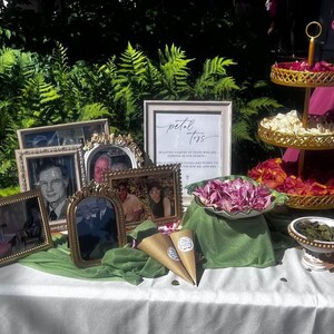 May include: A table decorated for a memorial service with a sign that reads "petal toss" in loving memory of those who are forever in our hearts. The table is decorated with flowers, photos, and small cones filled with petals.